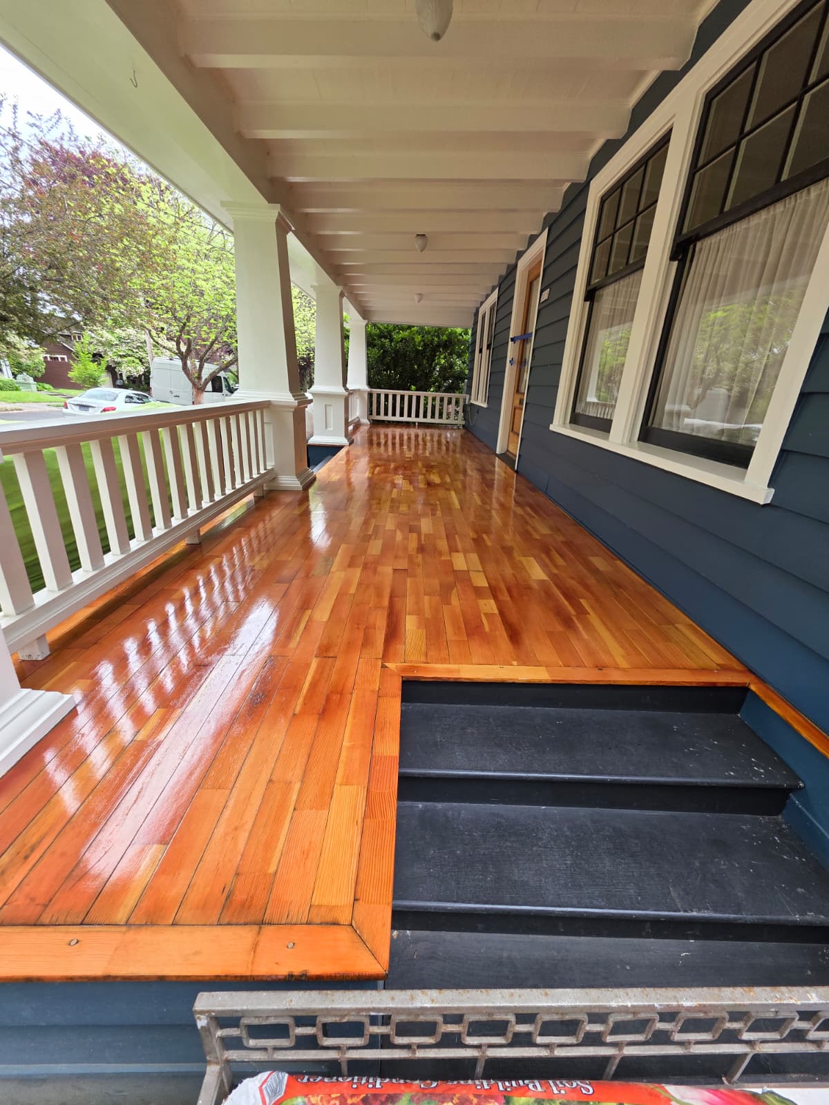 Refinished front porch with a glossy wood floor beside a navy blue home exterior