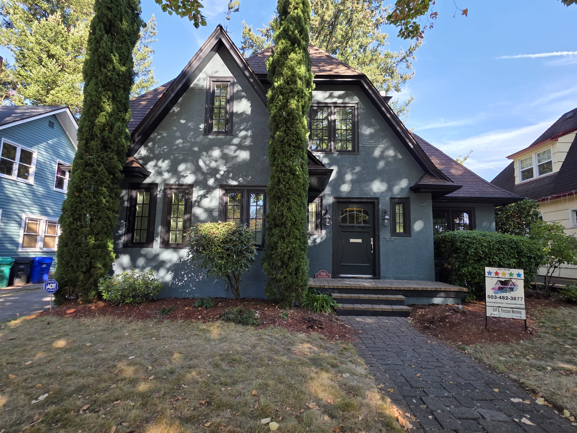 After: the same home repainted gray with dark trim and a Simply Pro Painting yard sign.